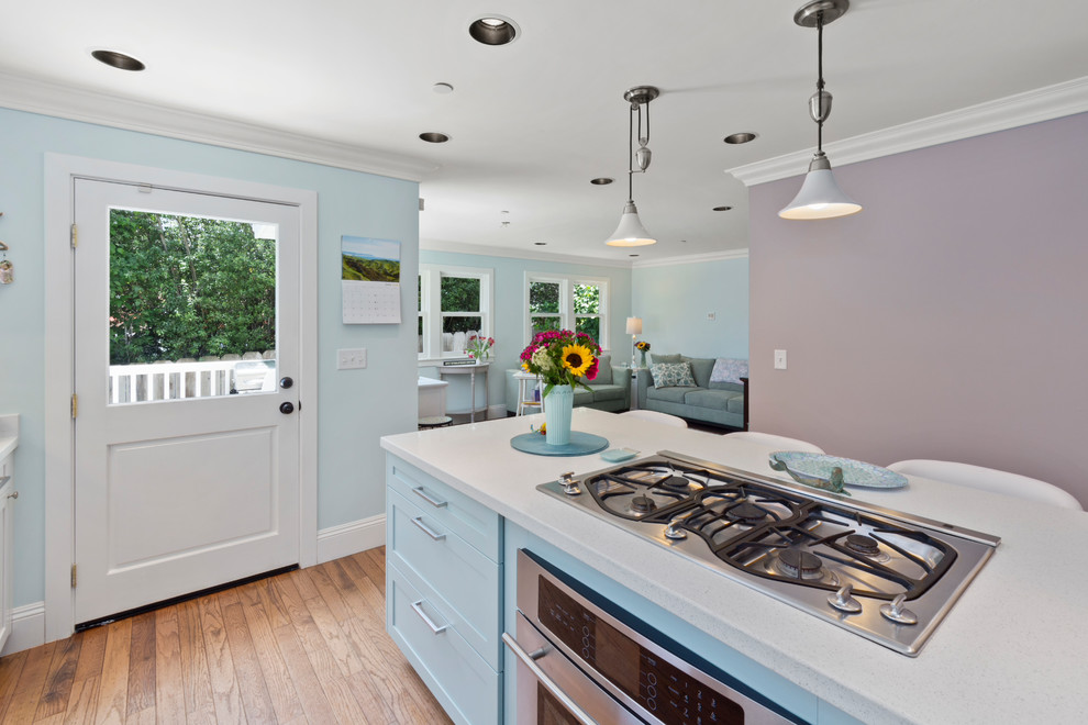 This is an example of a mid-sized beach style galley open plan kitchen in Other with a single-bowl sink, shaker cabinets, turquoise cabinets, quartz benchtops, white splashback, stainless steel appliances, medium hardwood floors, with island, brown floor and white benchtop.