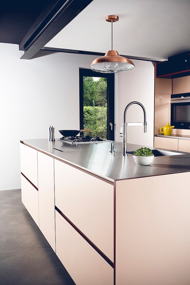 Industrial open plan kitchen in Dusseldorf with a drop-in sink, flat-panel cabinets, black appliances, concrete floors, with island, grey floor, beige cabinets, stainless steel benchtops and grey benchtop.