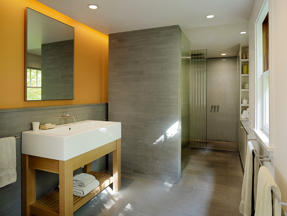 Contemporary bathroom in San Francisco with a trough sink, open cabinets, light wood cabinets, a curbless shower, gray tile and orange walls.