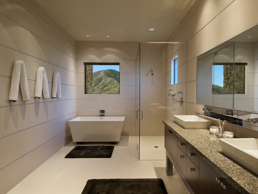 Photo of a large contemporary master bathroom in Phoenix with a vessel sink, flat-panel cabinets, dark wood cabinets, a freestanding tub, a corner shower, beige tile, granite benchtops, a one-piece toilet, glass tile, white walls and porcelain floors.