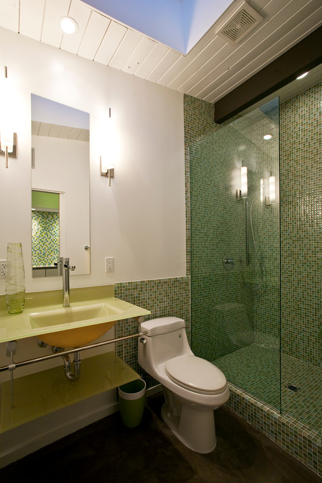 Photo of a mid-sized midcentury 3/4 bathroom in Other with a wall-mount sink, glass-front cabinets, glass benchtops, an open shower, a one-piece toilet, multi-coloured tile, white walls and concrete floors.