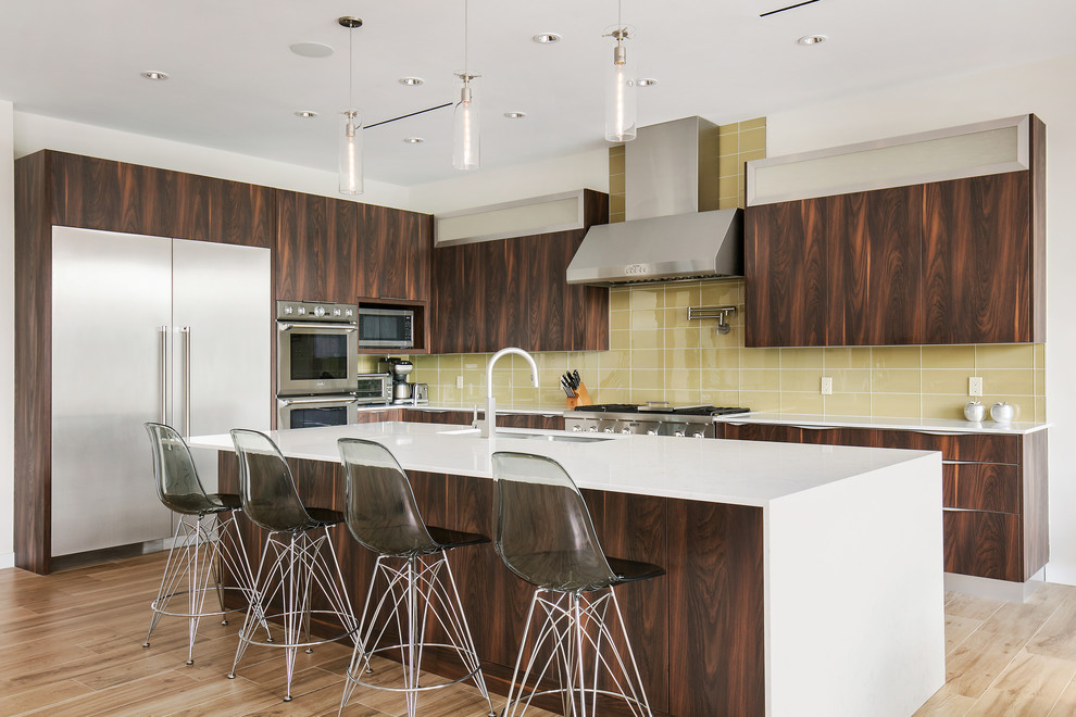 This is an example of a mid-sized contemporary l-shaped kitchen in Tampa with a double-bowl sink, flat-panel cabinets, dark wood cabinets, quartz benchtops, yellow splashback, glass tile splashback, stainless steel appliances, porcelain floors, with island, brown floor and white benchtop.