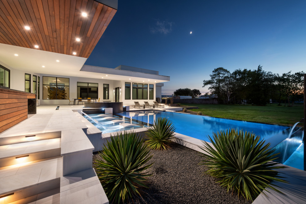 Ispirazione per una grande piscina a sfioro infinito minimalista rettangolare dietro casa con pavimentazioni in pietra naturale