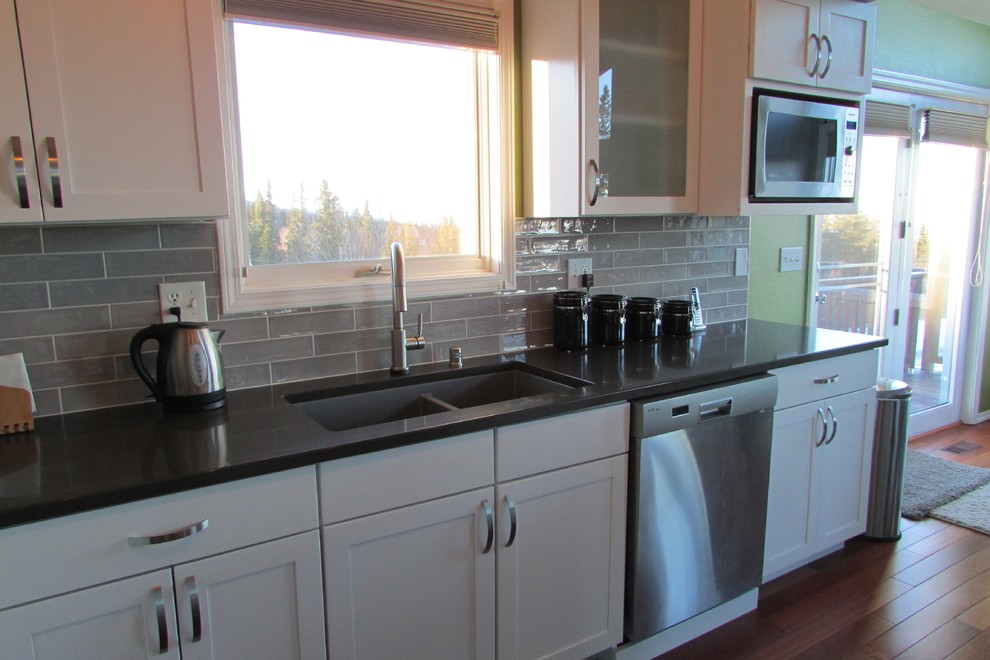 Mid-sized transitional l-shaped medium tone wood floor and brown floor eat-in kitchen photo with a double-bowl sink, recessed-panel cabinets, white cabinets, gray backsplash, stainless steel appliances, an island and subway tile backsplash