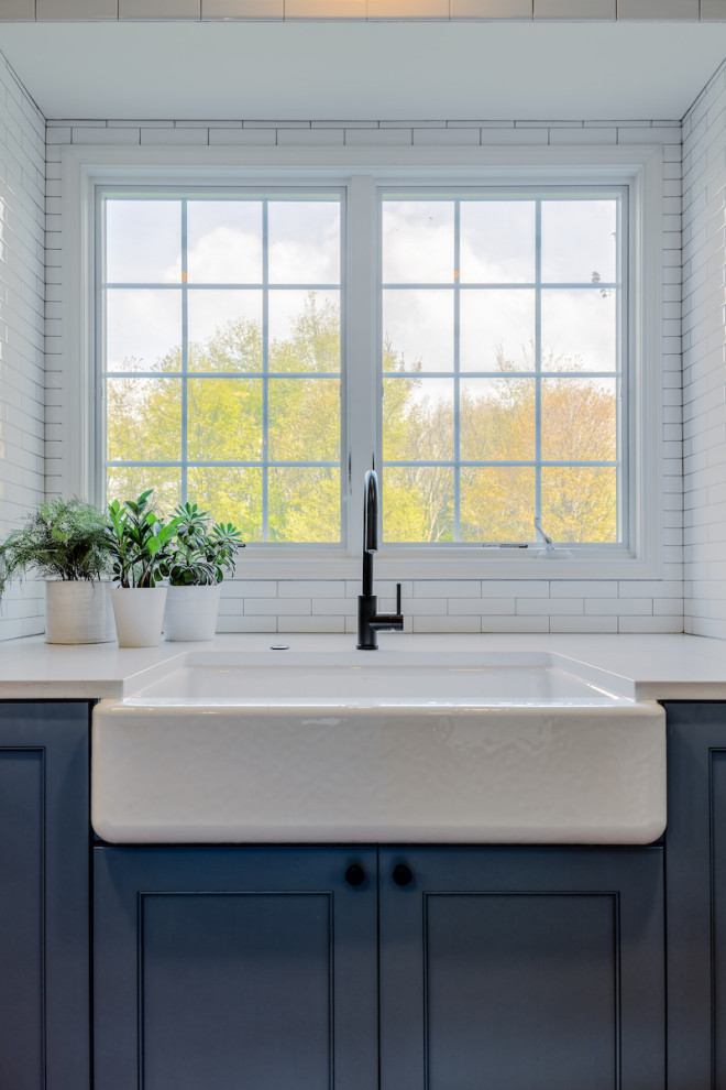 Transitional eat-in kitchen in Detroit with a farmhouse sink, shaker cabinets, blue cabinets, quartz benchtops, white splashback, ceramic splashback, stainless steel appliances, light hardwood floors, with island and white benchtop.