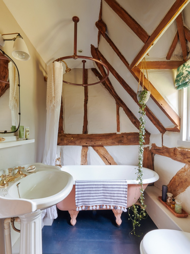 Inspiration for a medium sized rural family bathroom in Hampshire with a freestanding bath, a shower/bath combination, a wall mounted toilet, grey walls, dark hardwood flooring, a pedestal sink, black floors, a shower curtain, a single sink, exposed beams and brick walls.
