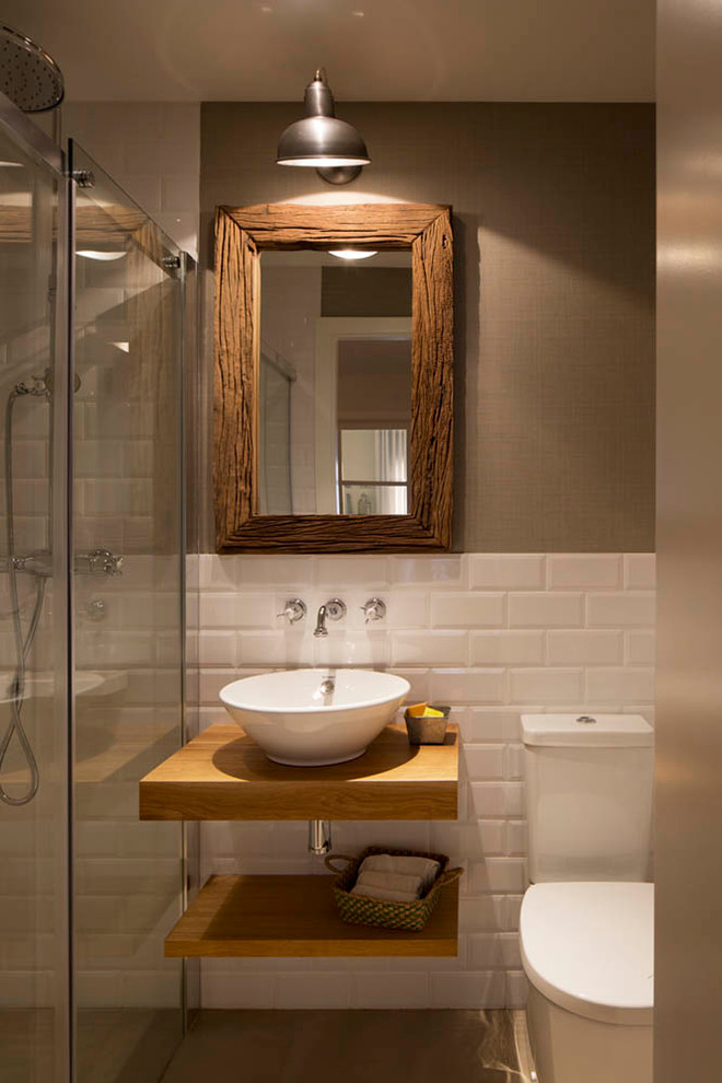 This is an example of a mid-sized country 3/4 bathroom in Barcelona with open cabinets, medium wood cabinets, an alcove shower, a two-piece toilet, white tile, ceramic tile, beige walls, a vessel sink, wood benchtops and brown benchtops.