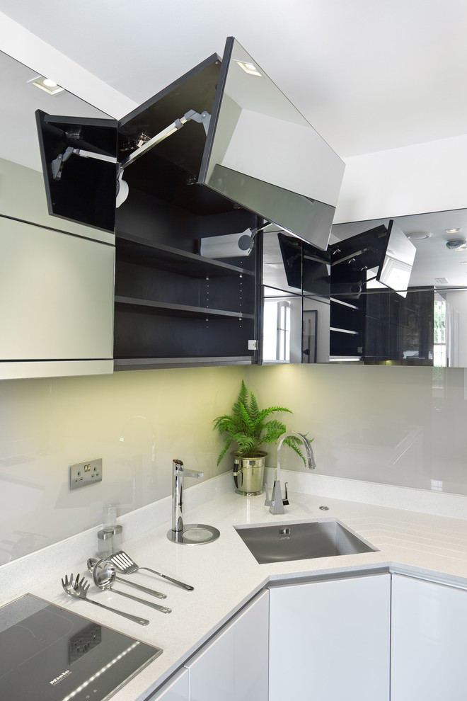 This is an example of a mid-sized contemporary single-wall eat-in kitchen in Hertfordshire with a drop-in sink, flat-panel cabinets, dark wood cabinets, solid surface benchtops, white splashback, glass sheet splashback, panelled appliances, ceramic floors and no island.