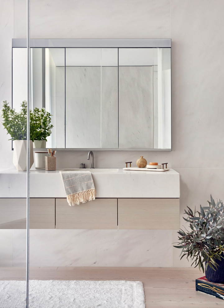 Photo of a large contemporary master bathroom in New York with flat-panel cabinets, light wood cabinets, white tile, beige tile, marble, light hardwood floors, marble benchtops, beige floor, white benchtops and an integrated sink.