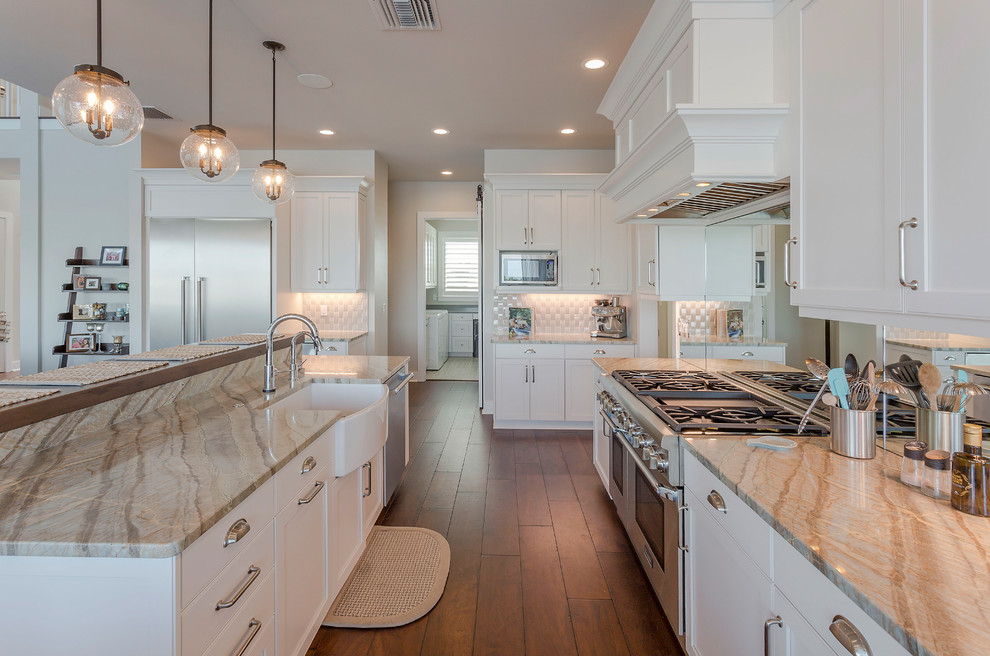 Inspiration for a mid-sized transitional galley open plan kitchen in Tampa with a farmhouse sink, recessed-panel cabinets, white cabinets, quartz benchtops, mirror splashback, stainless steel appliances, dark hardwood floors, with island, brown floor, white splashback and multi-coloured benchtop.
