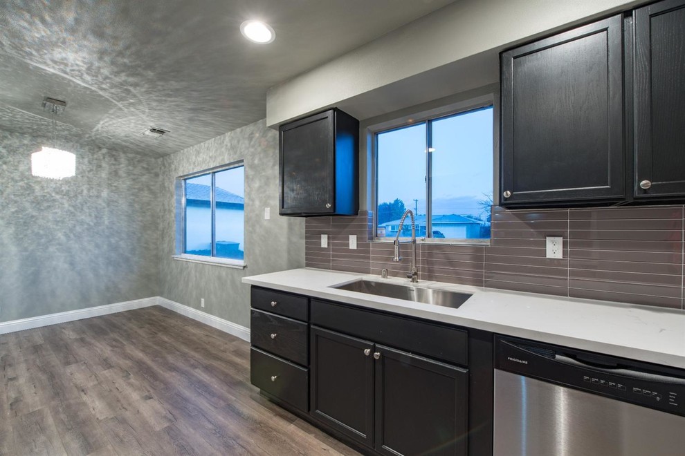 Large transitional galley dark wood floor and brown floor enclosed kitchen photo with an undermount sink, recessed-panel cabinets, black cabinets, quartz countertops, brown backsplash, glass sheet backsplash, stainless steel appliances and no island