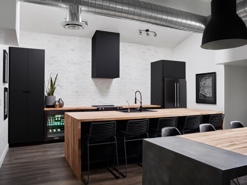 Contemporary galley eat-in kitchen in Phoenix with a drop-in sink, flat-panel cabinets, black cabinets, wood benchtops, white splashback, brick splashback, dark hardwood floors, with island, brown floor and beige benchtop.