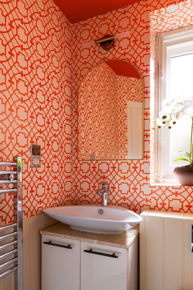 This is an example of a small eclectic powder room in London with orange walls and wallpaper.