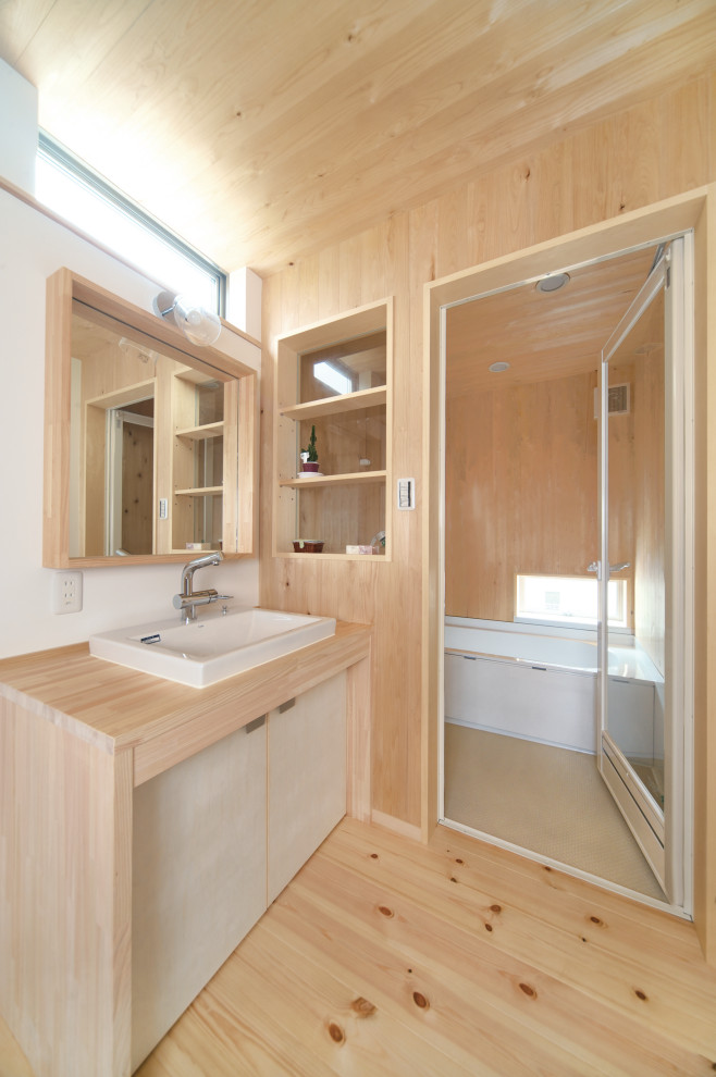 Photo of a mid-sized asian 3/4 bathroom in Kobe with flat-panel cabinets, beige cabinets, an alcove tub, beige walls, light hardwood floors, a drop-in sink, wood benchtops, beige floor, a hinged shower door and beige benchtops.