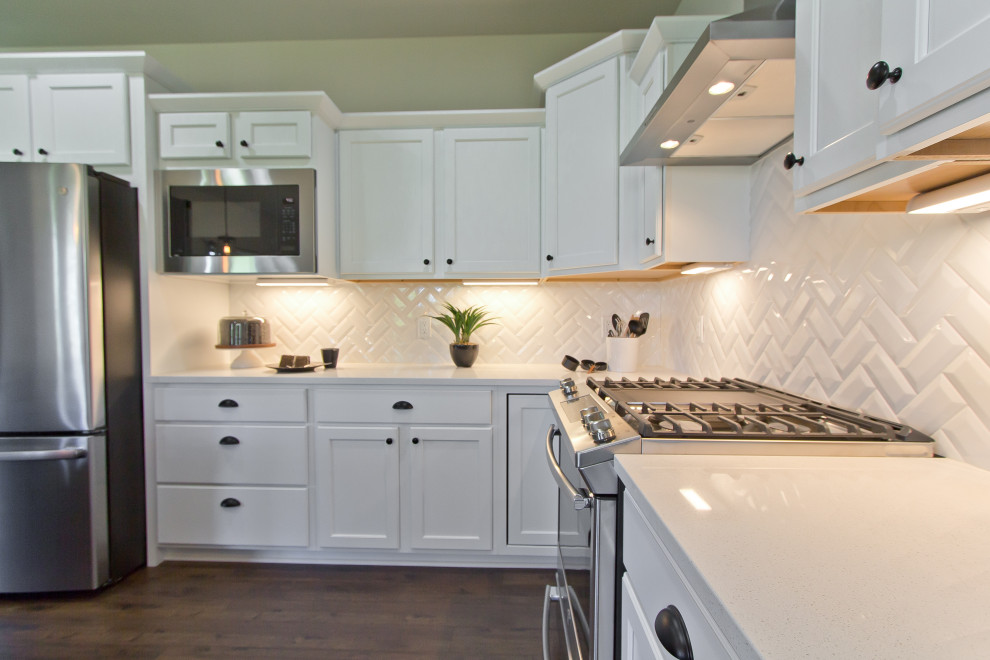 Example of a transitional l-shaped laminate floor and brown floor eat-in kitchen design with an undermount sink, recessed-panel cabinets, white cabinets, quartz countertops, white backsplash, subway tile backsplash, stainless steel appliances, an island and white countertops
