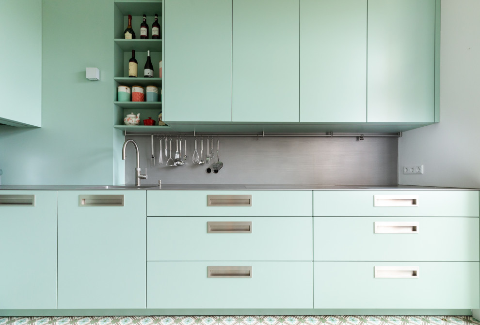 This is an example of a mid-sized contemporary l-shaped open plan kitchen in Frankfurt with an integrated sink, flat-panel cabinets, green cabinets, stainless steel benchtops, grey splashback, metal splashback, black appliances, turquoise floor and grey benchtop.