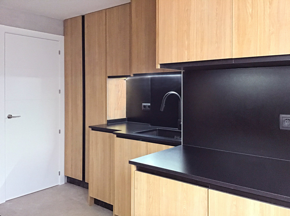 This is an example of a small l-shaped separate kitchen in Madrid with an undermount sink, medium wood cabinets, solid surface benchtops, black splashback, black appliances, porcelain floors, no island, beige floor and black benchtop.