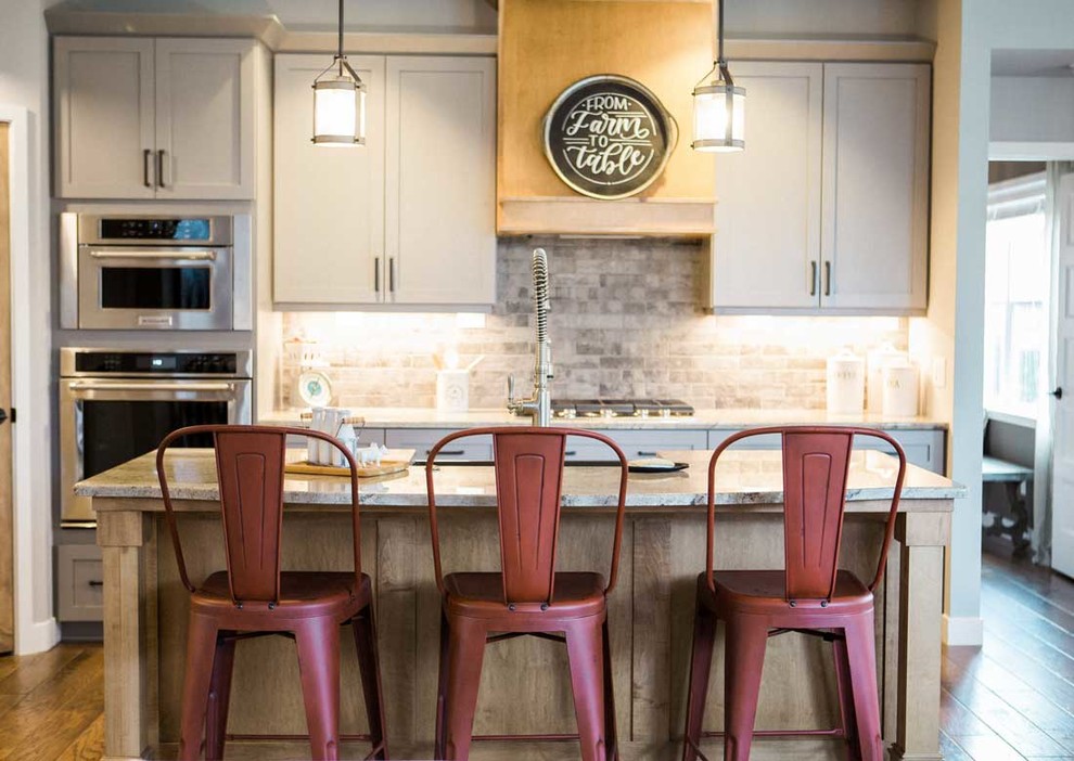 Example of a mid-sized transitional kitchen design with a farmhouse sink, granite countertops, gray backsplash, stainless steel appliances and an island