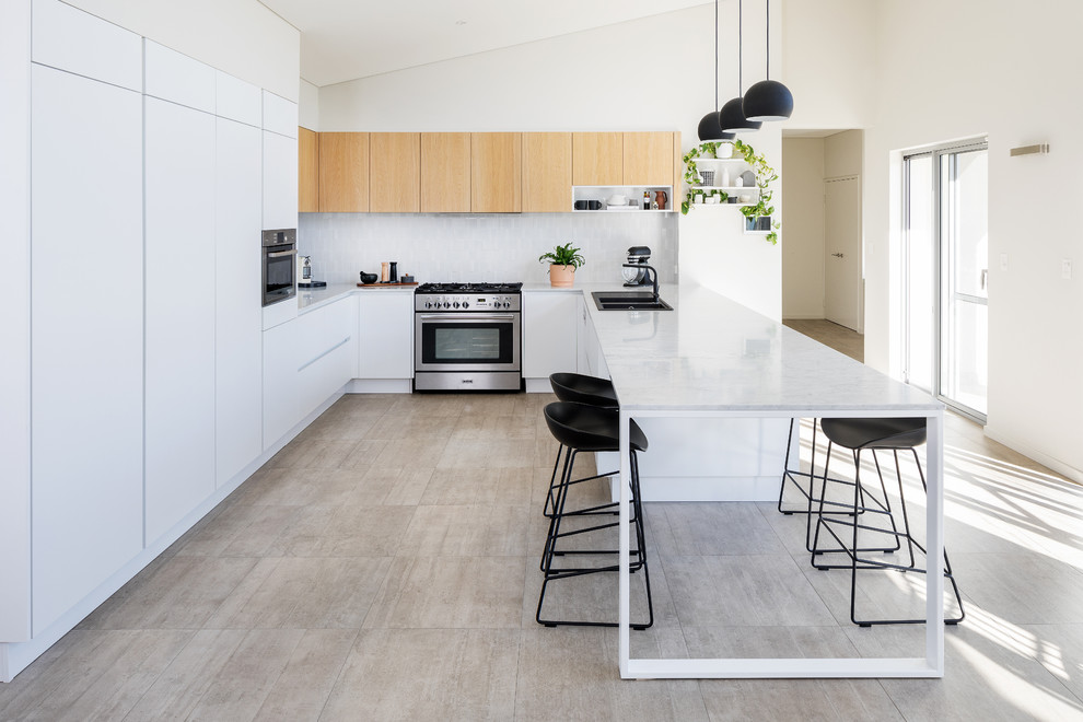 This is an example of a contemporary u-shaped kitchen in Perth with a drop-in sink, flat-panel cabinets, white cabinets, white splashback, panelled appliances, a peninsula, beige floor and grey benchtop.