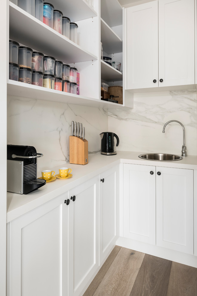 Inspiration for a large industrial galley open plan kitchen in Melbourne with a double-bowl sink, recessed-panel cabinets, white cabinets, quartz benchtops, white splashback, marble splashback, white appliances, medium hardwood floors, with island and grey floor.