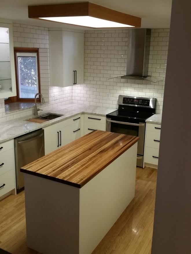 Inspiration for a mid-sized transitional brown floor kitchen remodel with an undermount sink, flat-panel cabinets, white cabinets, wood countertops, white backsplash, subway tile backsplash, stainless steel appliances and an island