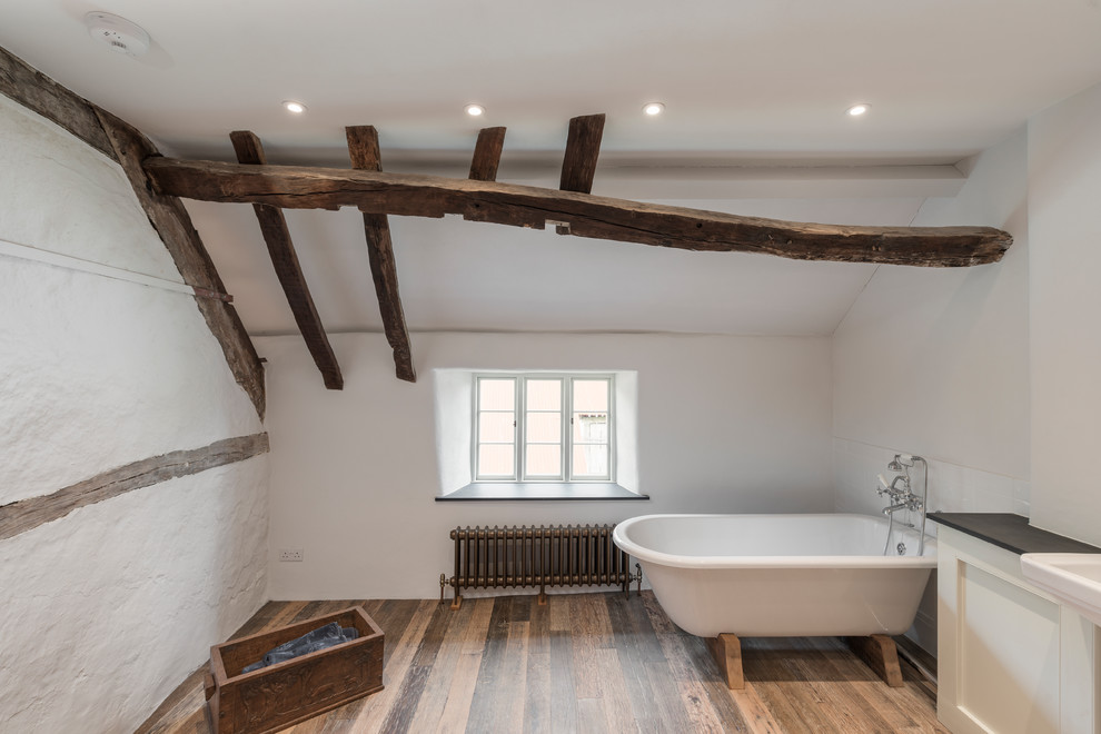 Inspiration for a small traditional master bathroom in Devon with recessed-panel cabinets, white cabinets, a freestanding tub, a curbless shower, a one-piece toilet, white tile, ceramic tile, white walls, medium hardwood floors, an integrated sink, brown floor and an open shower.