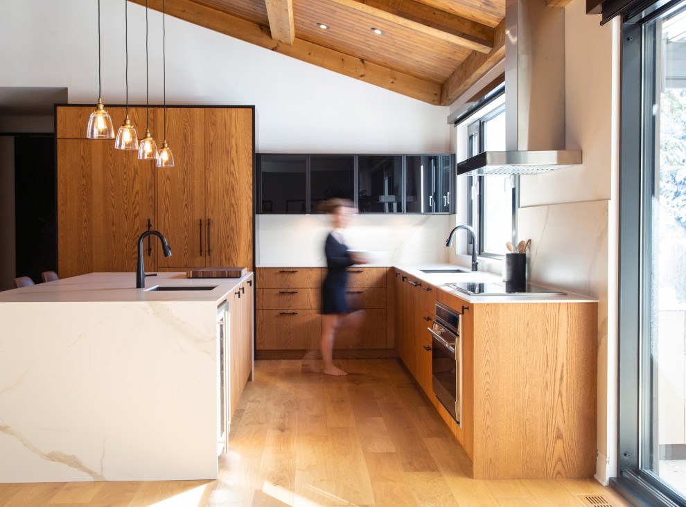 Mid-sized contemporary l-shaped kitchen in Montreal with an undermount sink, flat-panel cabinets, medium wood cabinets, white splashback, stainless steel appliances, medium hardwood floors, with island, white benchtop and exposed beam.