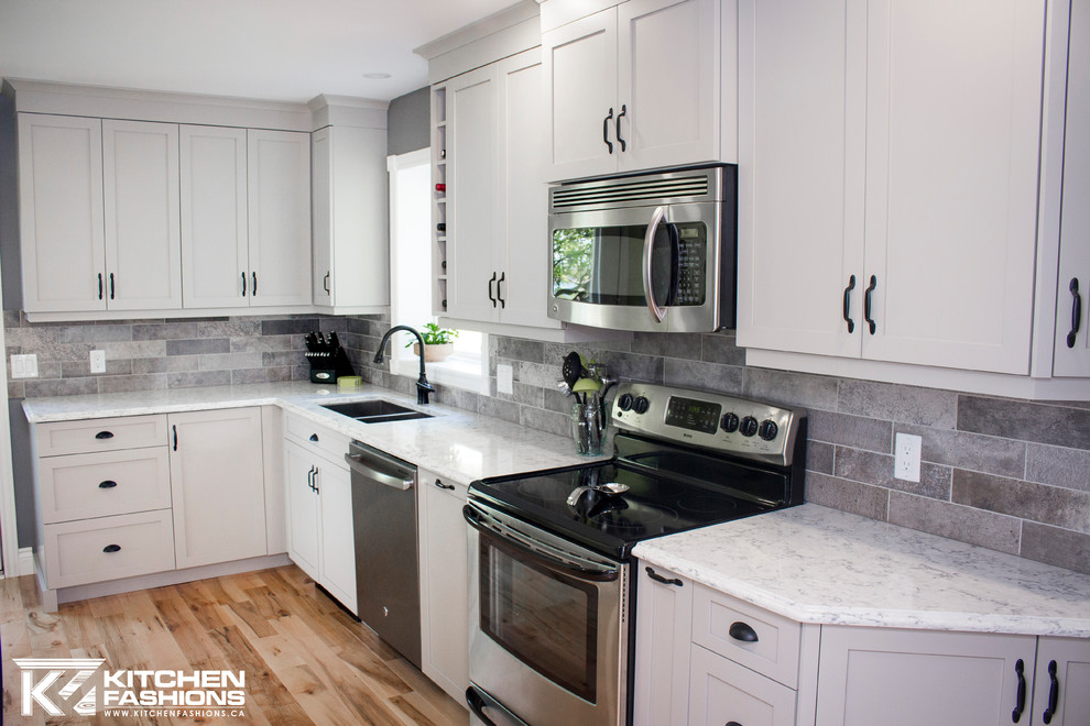 Eat-in kitchen - mid-sized contemporary galley light wood floor and brown floor eat-in kitchen idea with an undermount sink, shaker cabinets, gray cabinets, quartz countertops, gray backsplash, stone tile backsplash, stainless steel appliances and no island