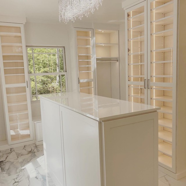 This is an example of a modern gender neutral walk-in wardrobe in Los Angeles with shaker cabinets, white cabinets, marble flooring and white floors.