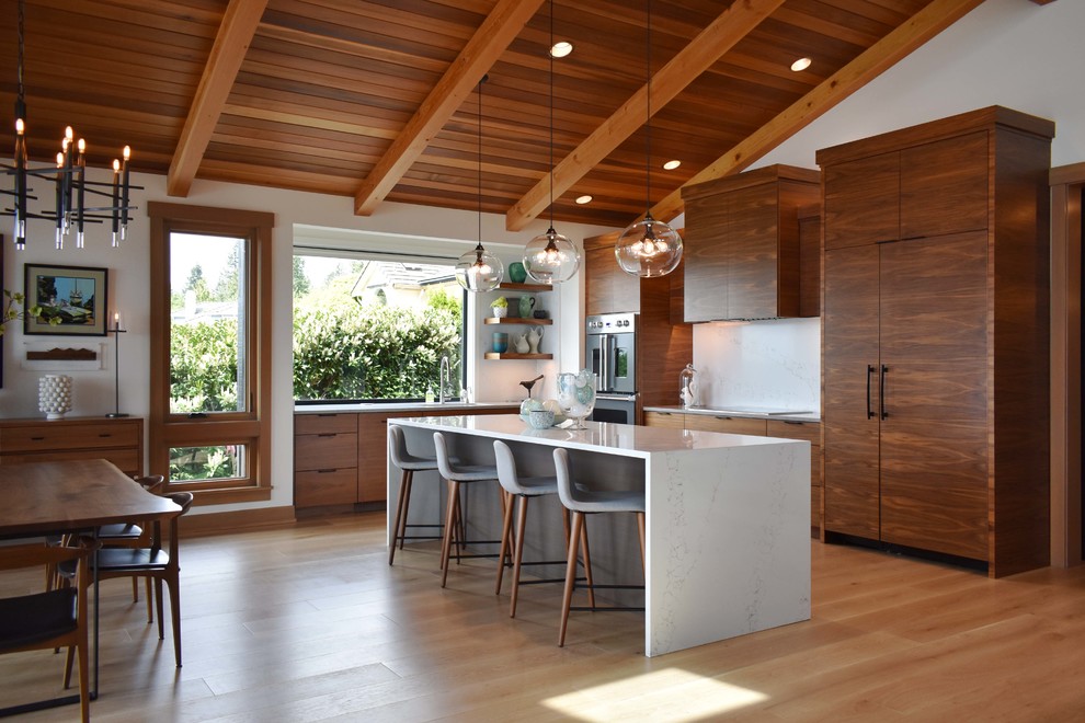 Design ideas for a country l-shaped kitchen in Seattle with flat-panel cabinets, medium wood cabinets, light hardwood floors, with island, white benchtop, white splashback, stone slab splashback, panelled appliances and beige floor.