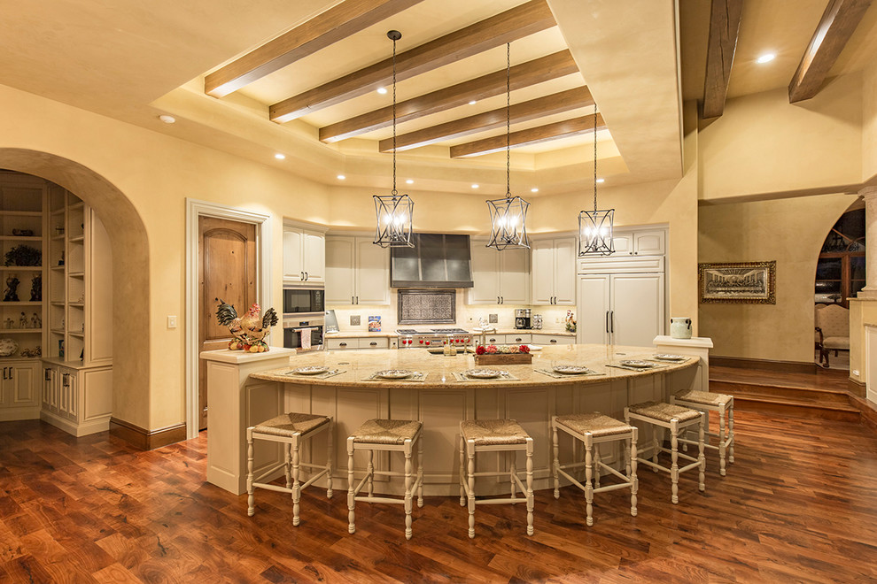 Inspiration for a large traditional single-wall open plan kitchen in Austin with an undermount sink, raised-panel cabinets, white cabinets, cement tile splashback, stainless steel appliances, medium hardwood floors, with island and beige benchtop.