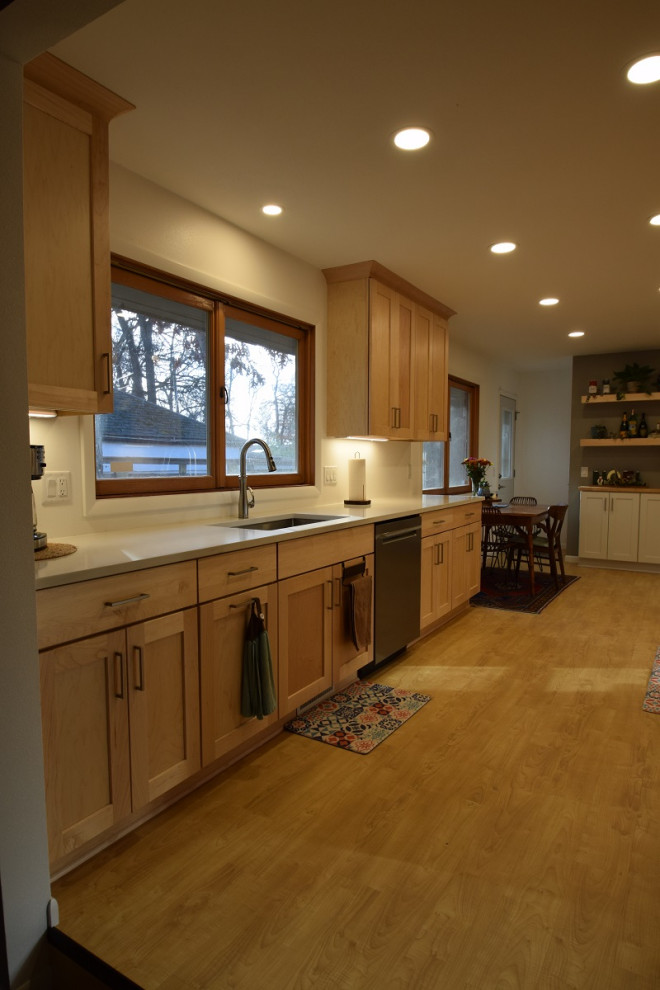 Example of a galley vinyl floor kitchen design with an undermount sink, shaker cabinets, light wood cabinets, quartz countertops, stainless steel appliances and white countertops