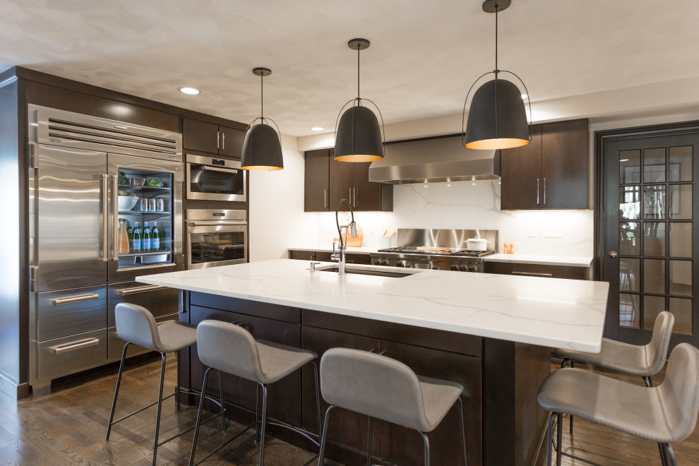 Photo of a large contemporary l-shaped eat-in kitchen in Boston with an undermount sink, flat-panel cabinets, black cabinets, solid surface benchtops, white splashback, stone slab splashback, stainless steel appliances, dark hardwood floors, with island, brown floor and white benchtop.