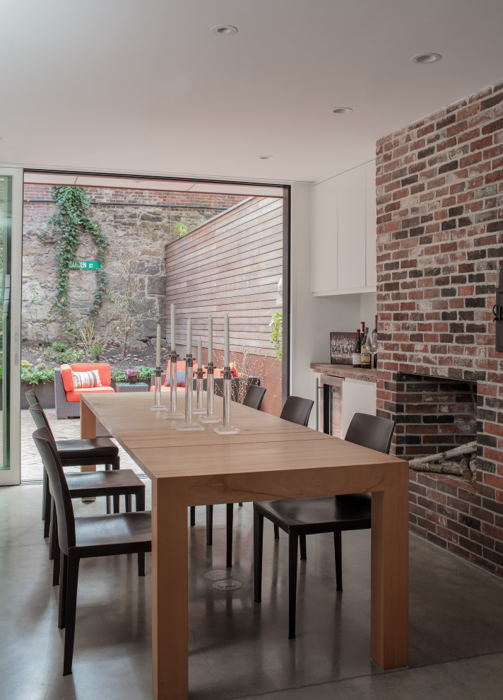 Inspiration pour une grande salle à manger ouverte sur la cuisine design avec un mur blanc, sol en béton ciré, un manteau de cheminée en brique et un sol gris.