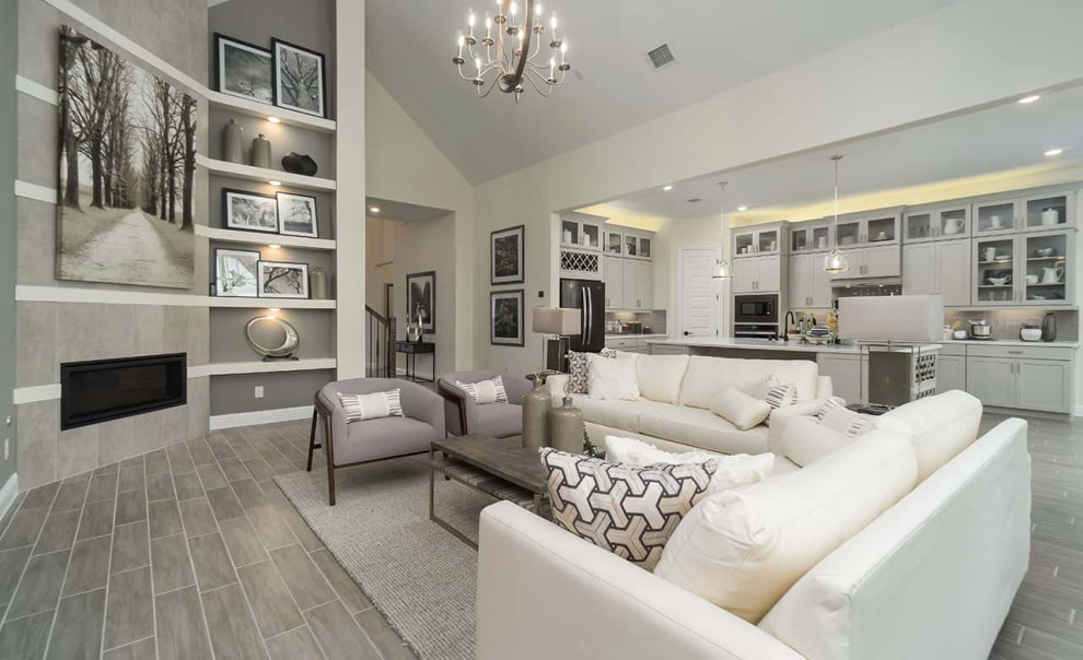 Photo of a contemporary open concept family room in Houston with grey walls, ceramic floors, a corner fireplace, a tile fireplace surround, grey floor and vaulted.