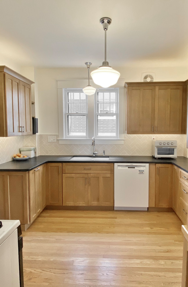 Small arts and crafts light wood floor enclosed kitchen photo with an undermount sink, recessed-panel cabinets, medium tone wood cabinets, soapstone countertops, beige backsplash, porcelain backsplash, white appliances and black countertops