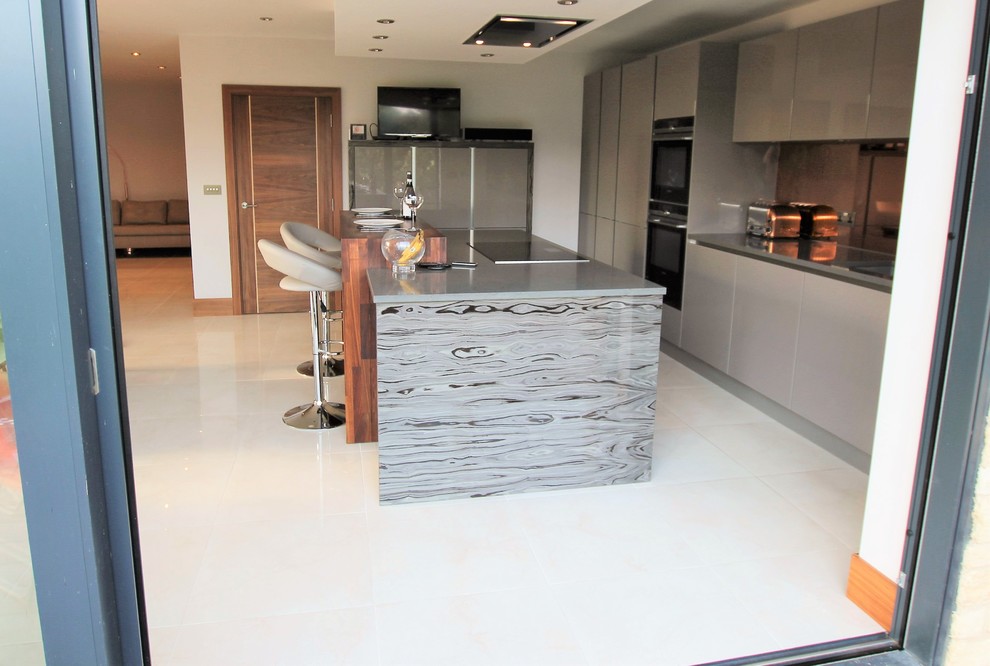 Photo of a large modern open plan kitchen in London with glass-front cabinets, grey cabinets, wood benchtops, metallic splashback, mirror splashback, black appliances, porcelain floors and with island.