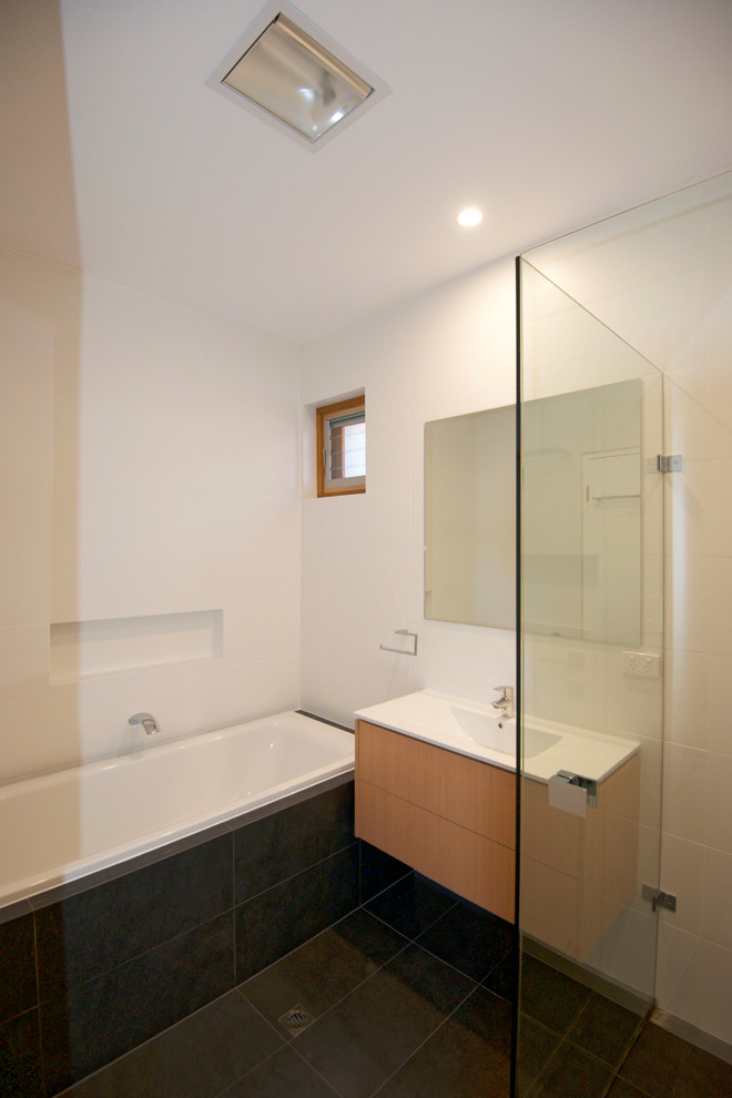 Small contemporary 3/4 bathroom in Adelaide with flat-panel cabinets, light wood cabinets, a drop-in tub, a corner shower, a wall-mount toilet, white tile, stone tile, white walls, slate floors, an integrated sink and solid surface benchtops.