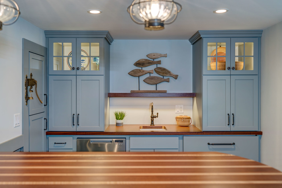 This is an example of a mid-sized beach style galley seated home bar in Boston with an undermount sink, shaker cabinets, blue cabinets, wood benchtops, porcelain floors and grey floor.