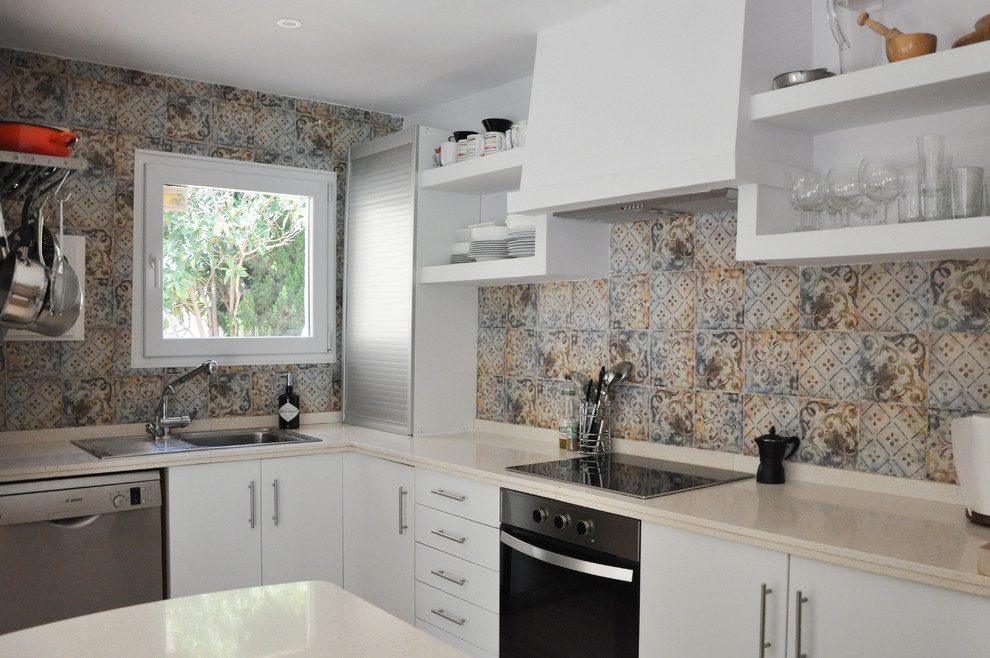Mediterranean l-shaped eat-in kitchen in Alicante-Costa Blanca with a drop-in sink, flat-panel cabinets, white cabinets, solid surface benchtops, multi-coloured splashback, ceramic splashback, stainless steel appliances, ceramic floors, a peninsula and beige floor.