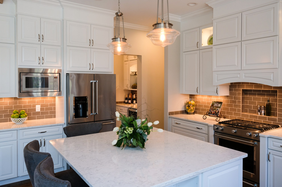 Example of a large transitional u-shaped eat-in kitchen design with raised-panel cabinets, white cabinets, quartz countertops, brown backsplash, stainless steel appliances and an island