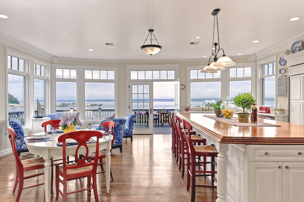 Photo of a large beach style single-wall eat-in kitchen in Seattle with raised-panel cabinets, white cabinets, wood benchtops, panelled appliances, medium hardwood floors and with island.