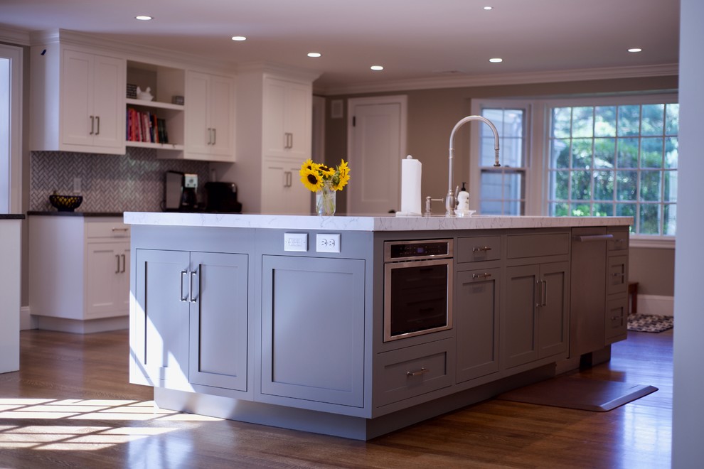 Country l-shaped eat-in kitchen in Boston with an undermount sink, shaker cabinets, grey cabinets, quartz benchtops, white splashback, ceramic splashback, stainless steel appliances, dark hardwood floors, with island and brown floor.