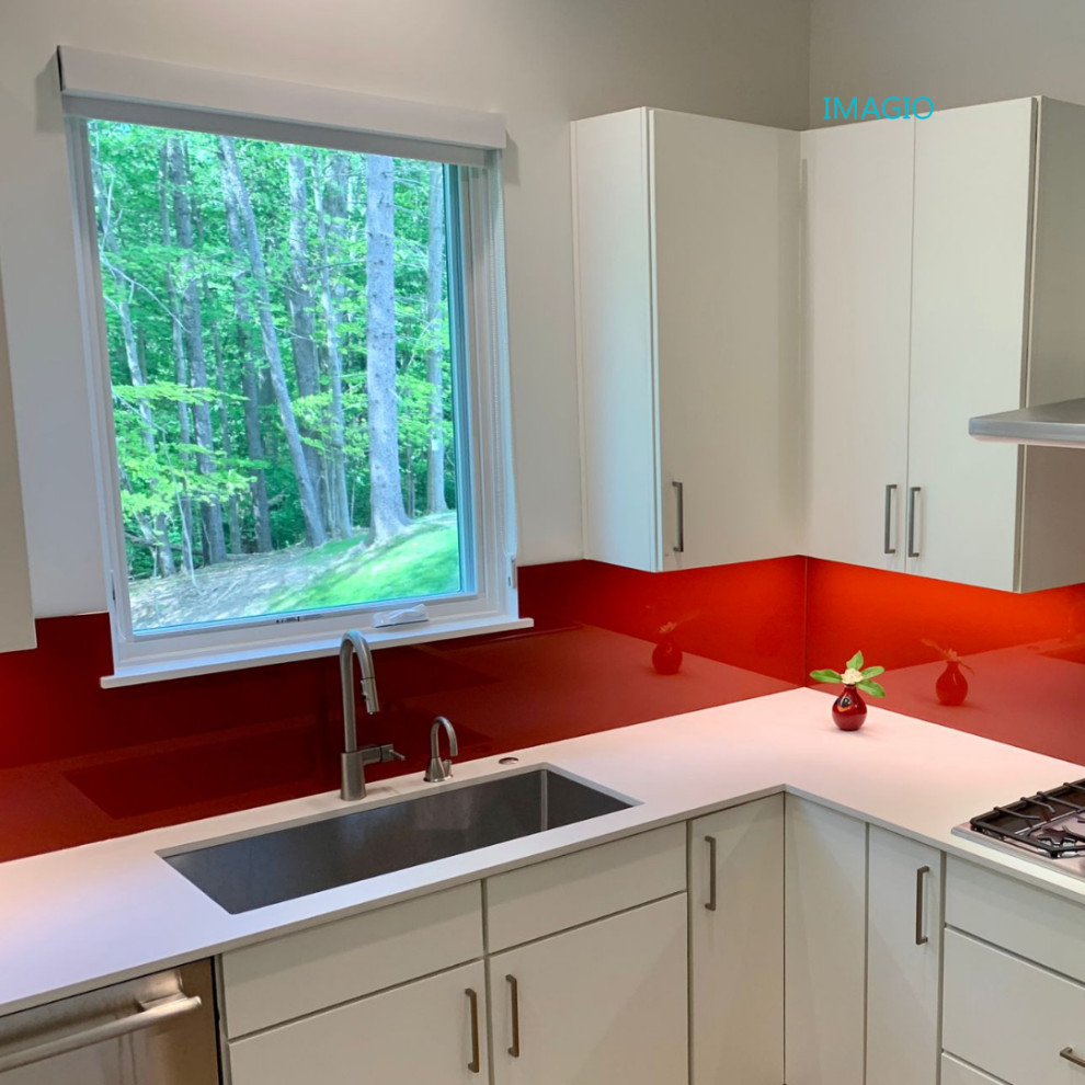 Cette photo montre une cuisine tendance avec un placard à porte plane, une crédence rouge, une crédence en feuille de verre, îlot et un plan de travail blanc.