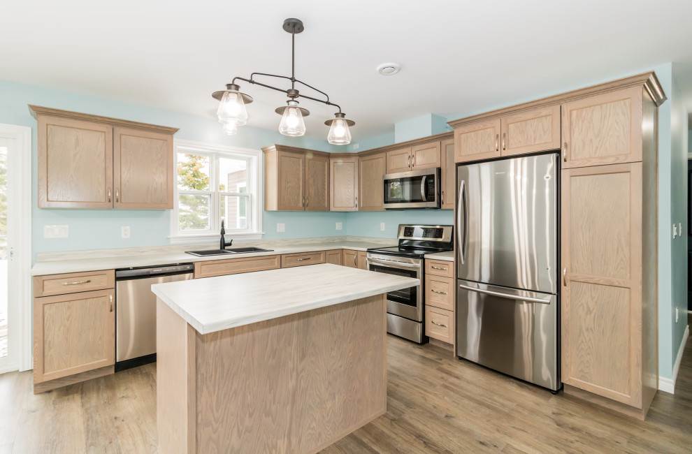 Inspiration for a mid-sized l-shaped laminate floor and brown floor kitchen remodel with a double-bowl sink, recessed-panel cabinets, light wood cabinets, laminate countertops, stainless steel appliances, an island and white countertops