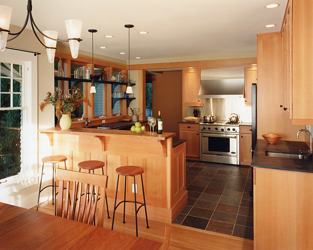 Photo of a mid-sized arts and crafts u-shaped eat-in kitchen in Seattle with an undermount sink, recessed-panel cabinets, light wood cabinets, solid surface benchtops, beige splashback, metal splashback, stainless steel appliances, slate floors and a peninsula.