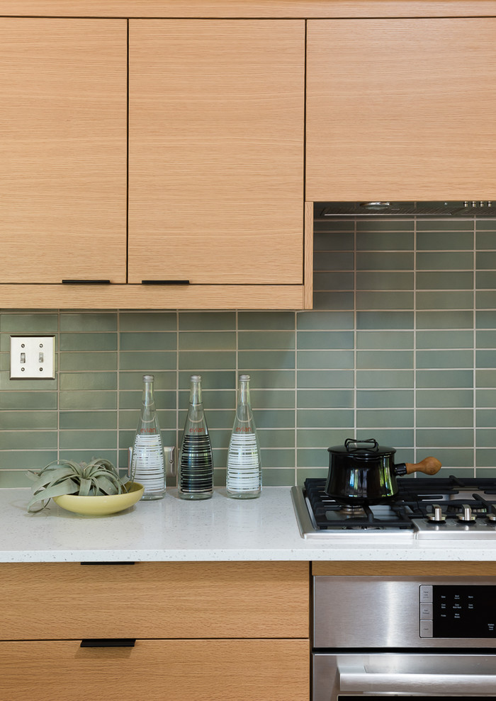 Bild på ett mellanstort retro kök, med en undermonterad diskho, släta luckor, skåp i mellenmörkt trä, bänkskiva i kvarts, grönt stänkskydd, stänkskydd i keramik, rostfria vitvaror, klinkergolv i porslin, en köksö och grått golv