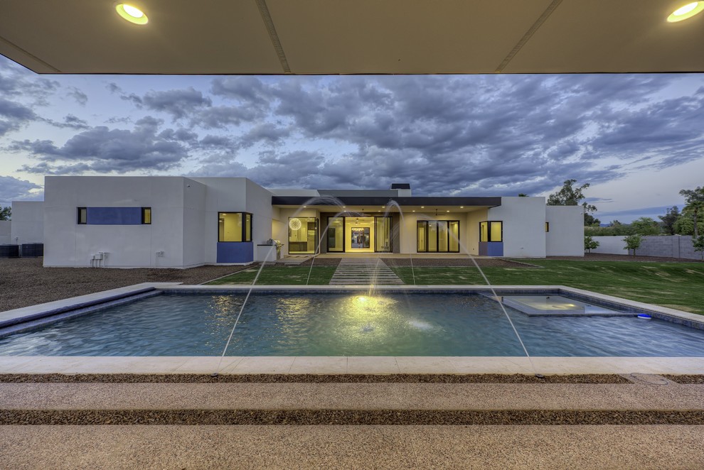 This is an example of a mid-sized modern backyard rectangular lap pool in Phoenix with a water feature and concrete pavers.