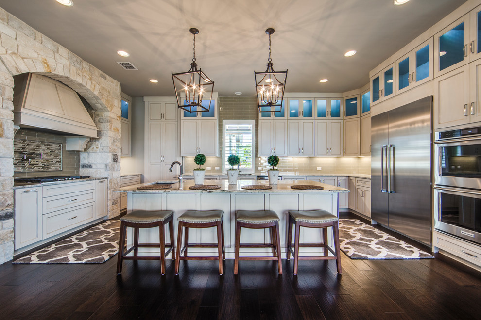 Traditional u-shaped kitchen in Dallas with a single-bowl sink, shaker cabinets, marble benchtops, beige splashback, glass tile splashback, stainless steel appliances, dark hardwood floors, with island, beige cabinets and brown floor.