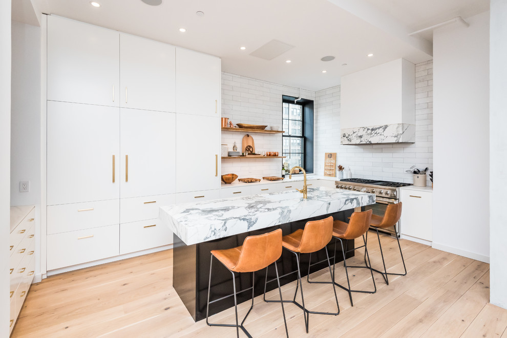 This is an example of a contemporary l-shaped kitchen in New York with an undermount sink, flat-panel cabinets, white cabinets, white splashback, stainless steel appliances, light hardwood floors and with island.